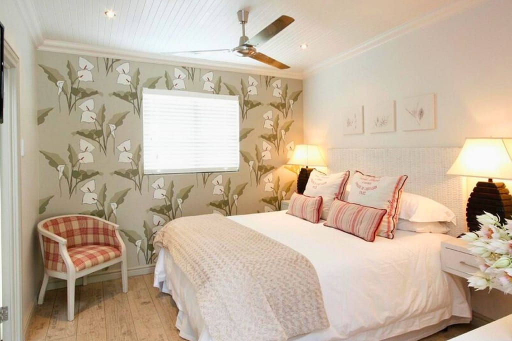 Gemütliches Schlafzimmer mit Doppelbett, floraler Tapete, kariertem Sessel und warmen Nachttischlampen.