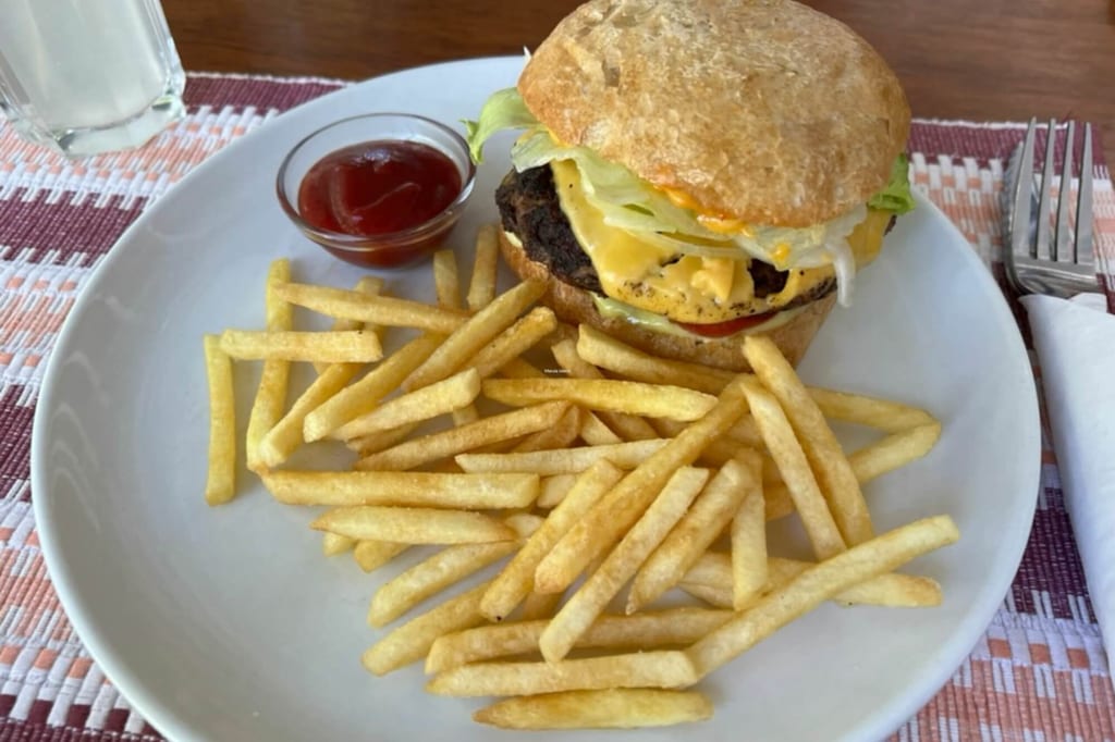 Cheeseburger mit geschmolzenem Käse und Pommes frites auf weißem Teller, Schälchen Ketchup daneben.