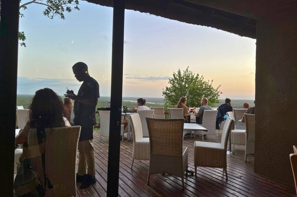 Blick auf eine Terrasse mit Gästen und silhouettiertem Kellner bei Sonnenuntergang