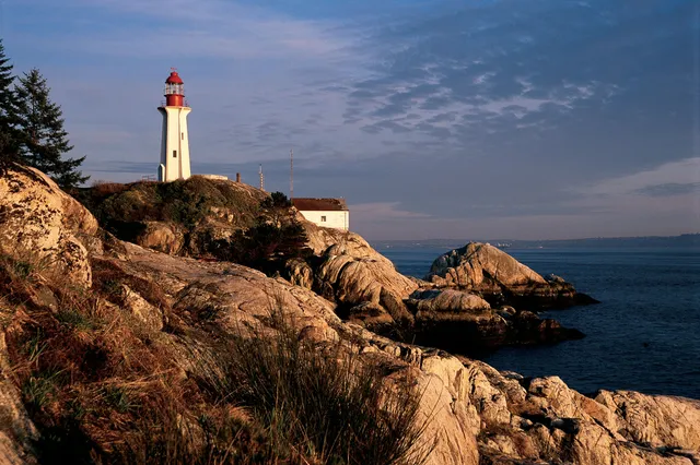 Leuchtturm auf einer felsigen Küste im warmen Abendlicht, ruhiges Meer und weiter Himmel
