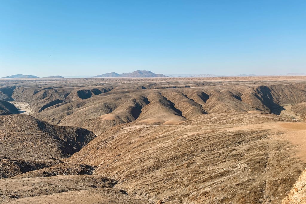 Weite, trockene Hügellandschaft mit klar blauem Himmel und erdigen Tönen