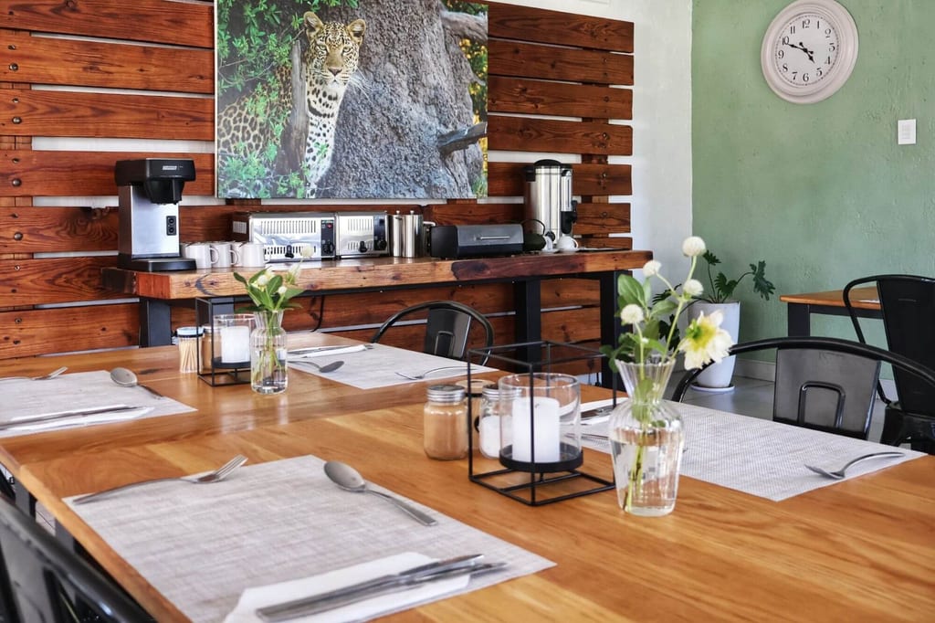 Gedeckte Holztische mit Blumen, Buffet und großes Tierbild an der Wand, freundlicher Tageslichtraum.