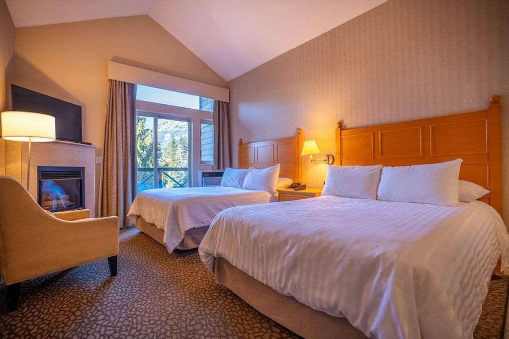 Gemütliches Doppelzimmer mit zwei Betten, Kamin und Bergblick durch die Balkontür.