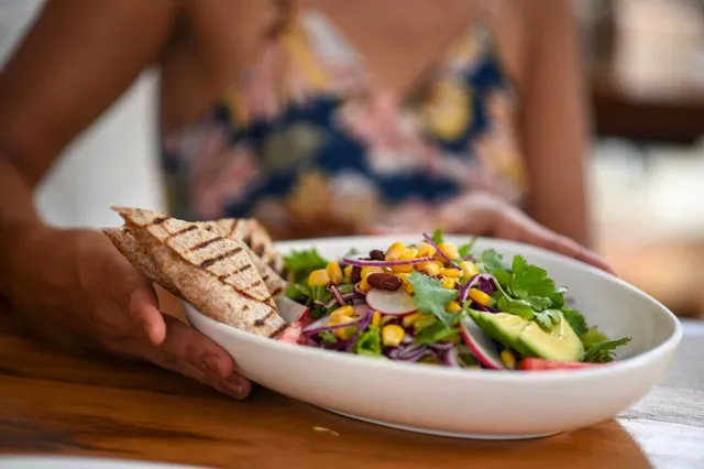 Nahaufnahme einer Schüssel mit buntem Salat und gegrilltem Fladenbrot, von einer Hand gehalten.
