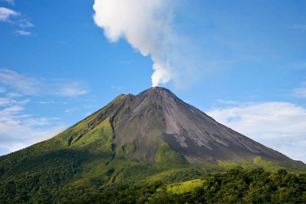 Vulkan Arenal in Costa Rica mit weißer Rauchfahne über grünem Regenwald unter blauem Himmel