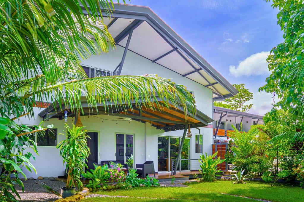 Modernes Einfamilienhaus mit überdachter Terrasse und tropischem Garten bei sonnigem Wetter