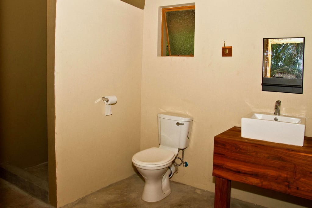 Ein einfaches Badezimmer mit WC, Waschbecken auf Holzkonsole und kleinem Fenster.