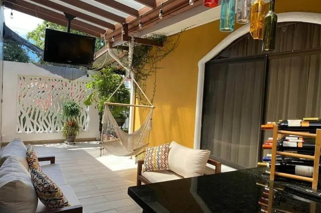 Gemütliche überdachte Terrasse mit Sofas, Hängesessel, Weinregal und Pflanzen bei Tageslicht.