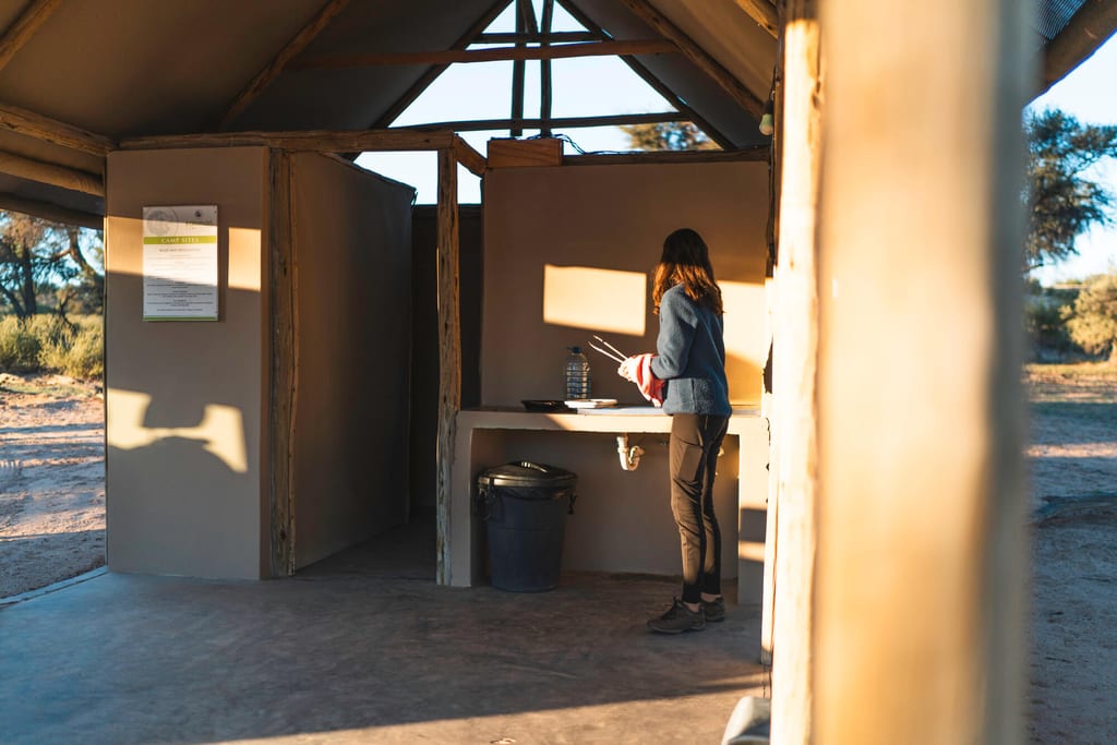 Person an einem offenen Camping-Waschplatz im warmen Abendlicht, seitliche Perspektive