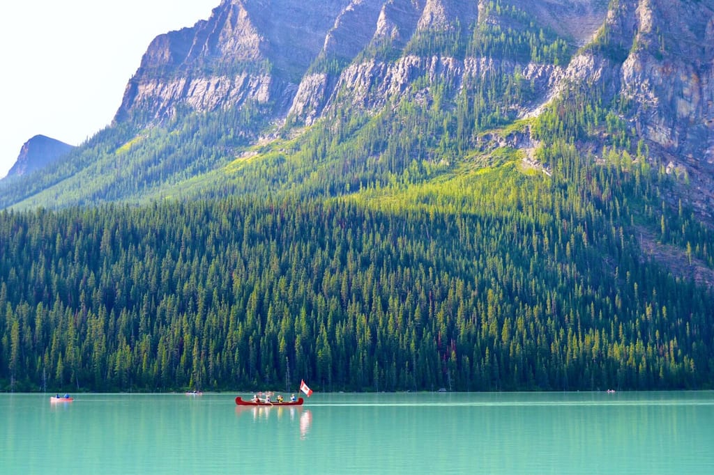 Auf dem Lake Louise fährt ein Kanu vor Wald und Bergkulisse entlang