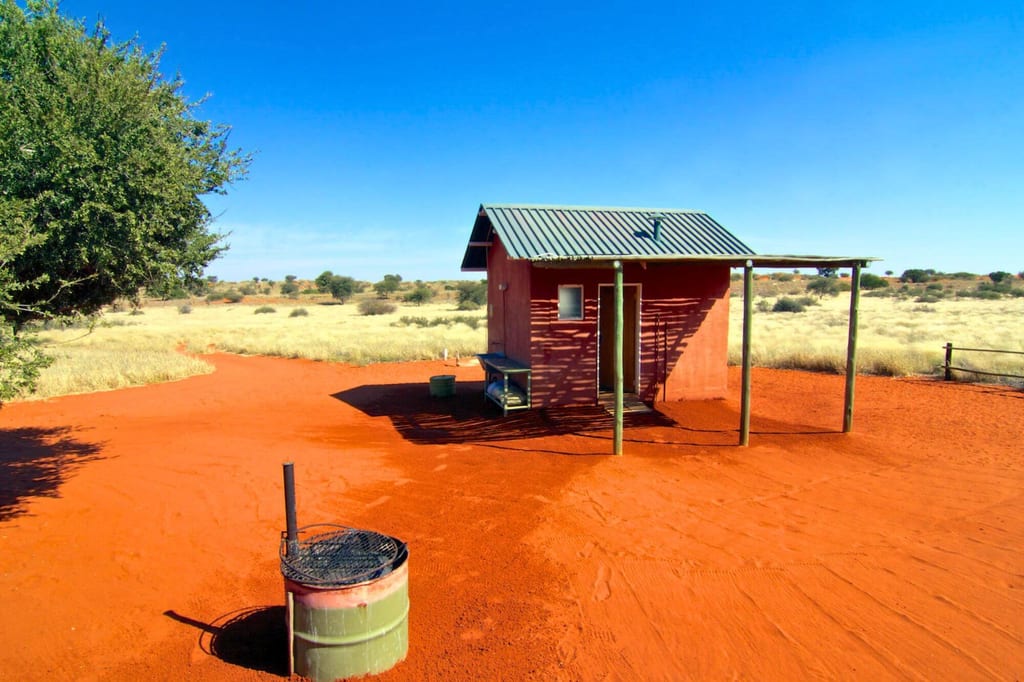 Einfache Hütte auf rotem Sandboden in trockener, sonniger Landschaft mit blauem Himmel