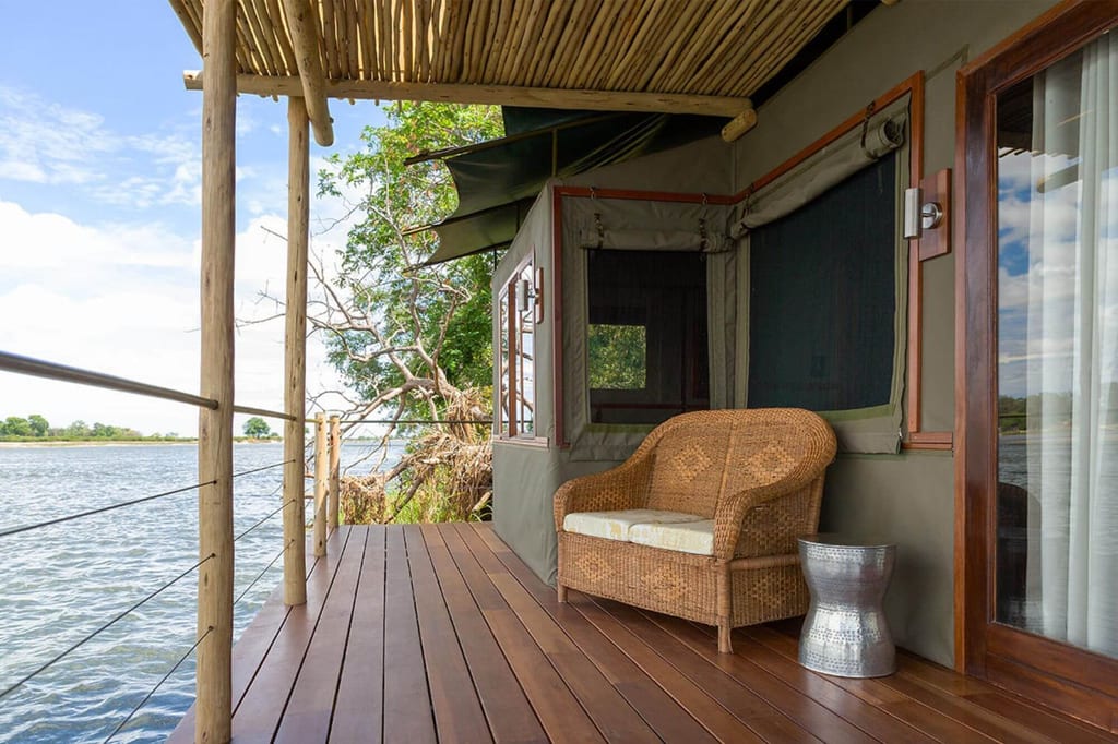Veranda eines Safari-Zeltes mit geflochtenem Sessel über einem ruhigen Fluss