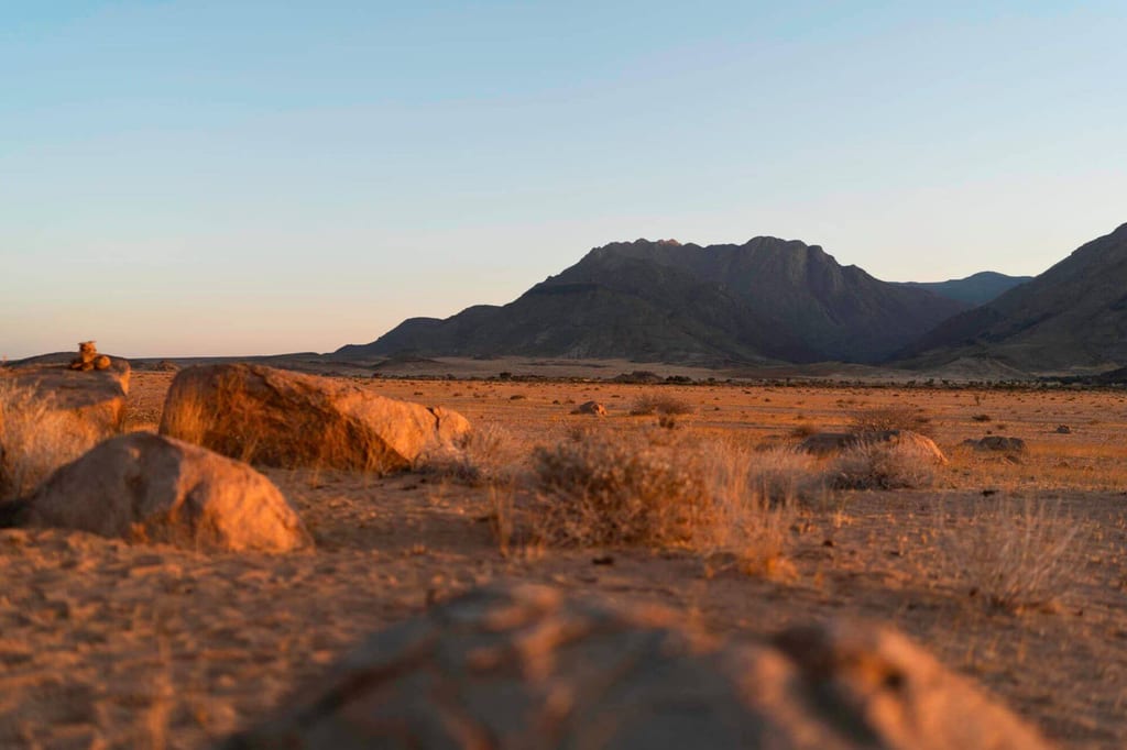 Weite Fels- und Grassteppe im Damaraland bei goldenem Abendlicht, Bergkette am Horizont.