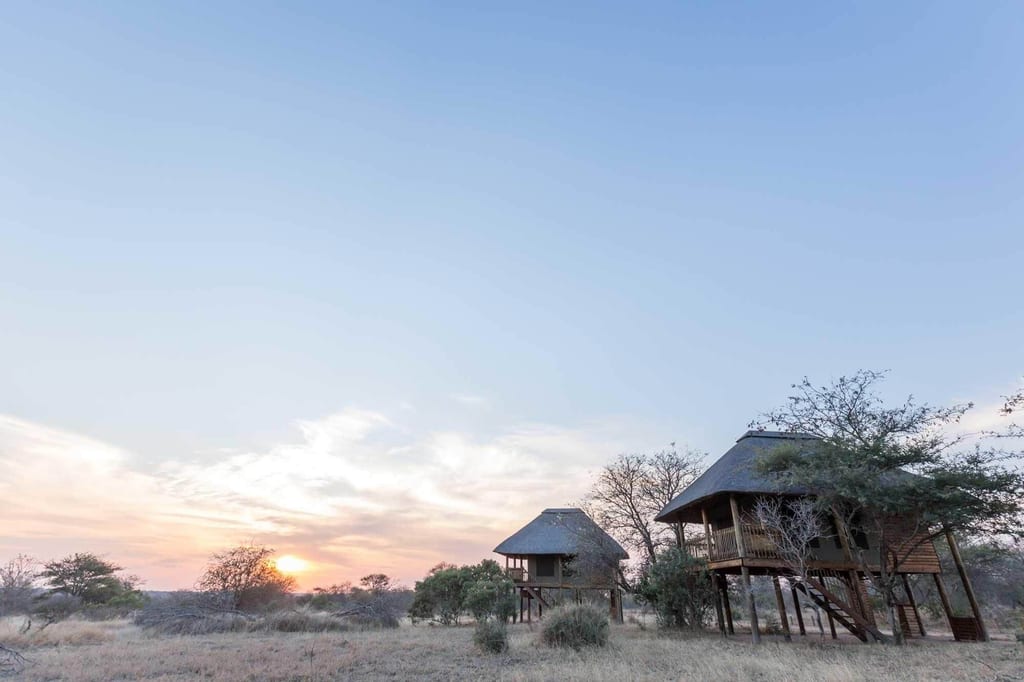 Zwei erhöhte Safari-Bungalows in trockener Savannenlandschaft bei tiefstehender Sonne