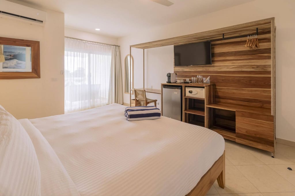 Helles Hotelzimmer mit großem Doppelbett, Holzmöbelwand und Tageslicht durch Vorhang