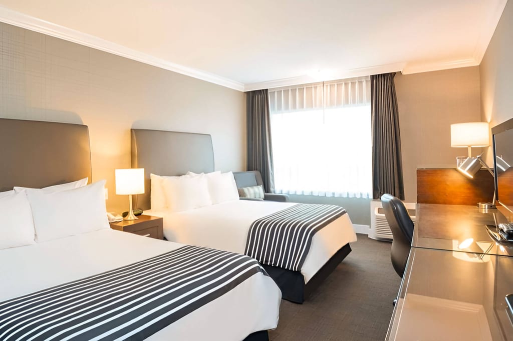 Helles Hotelzimmer mit zwei Doppelbetten, Schreibtisch und großem Fenster