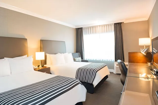 Helles Hotelzimmer mit zwei Doppelbetten, Schreibtisch und großem Fenster
