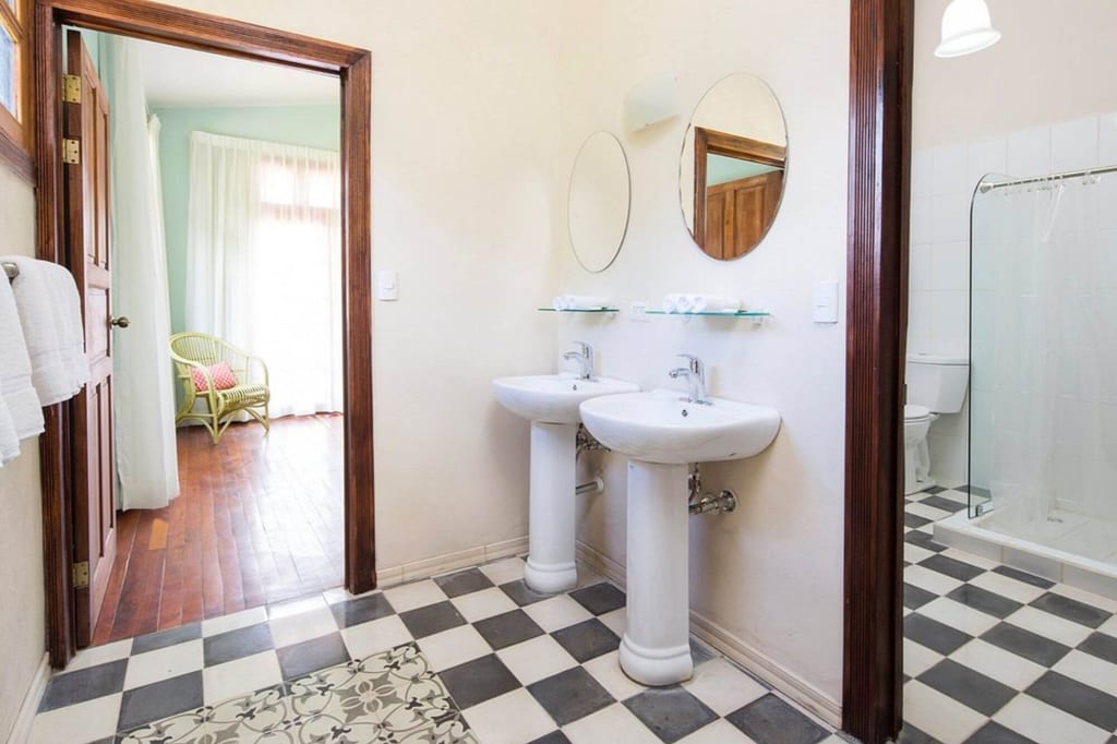 Helles Badezimmer mit zwei Standwaschbecken, runden Spiegeln und schwarz-weiß kariertem Boden, Blick in angrenzenden Raum
