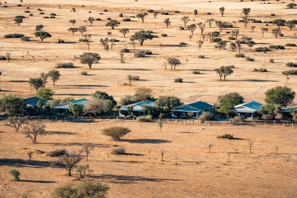 Vogelperspektive auf Lodges in trockener Savannenlandschaft bei warmem Nachmittagslicht.