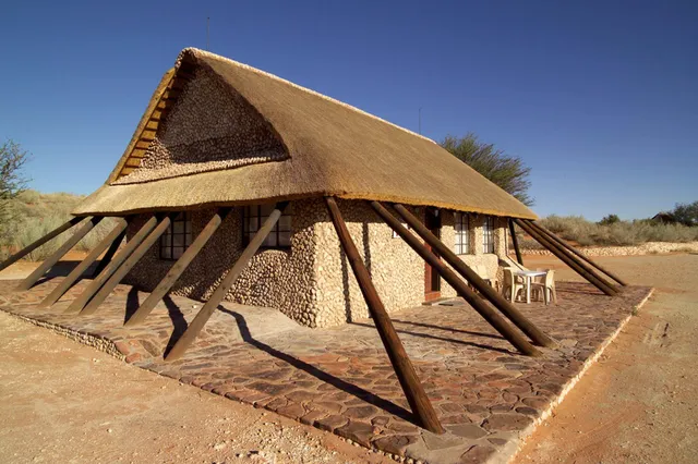 Kleines Haus mit Reetdach und schrägen Holzstützen in trockener Landschaft bei warmem Seitenlicht.