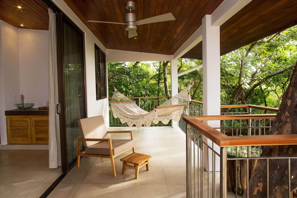 Überdachte Terrasse mit Hängematte und Holzsessel vor grünen Bäumen
