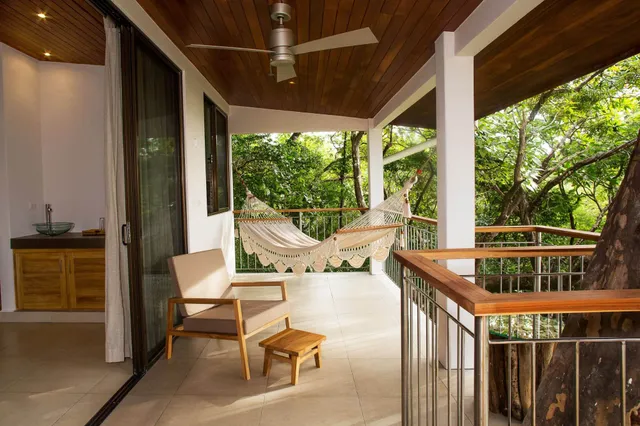 Überdachte Terrasse mit Hängematte und Holzsessel vor grünen Bäumen