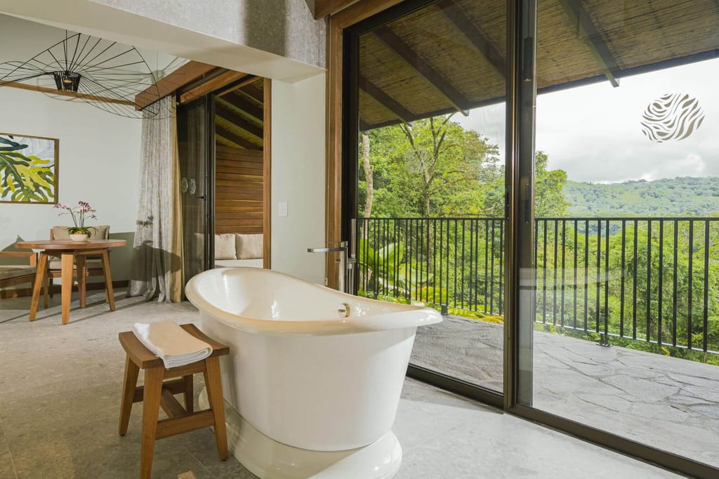 Freistehende Badewanne im Zimmer mit Balkon und Blick auf grüne Hügel und Wald