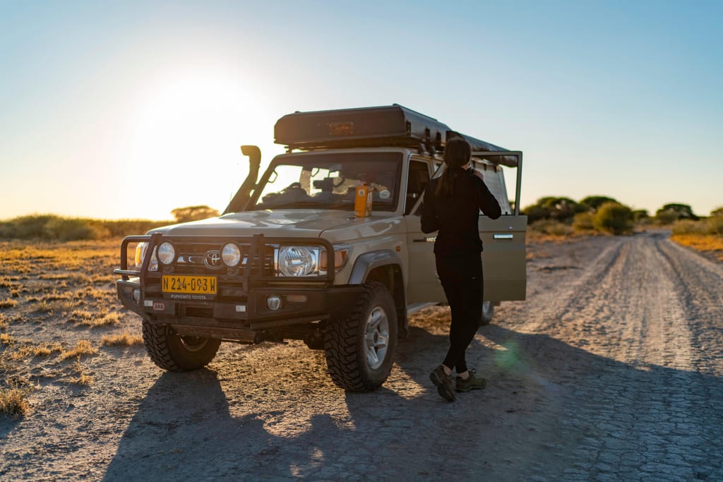 Geländewagen auf trockener Piste bei tief stehender Sonne, Person steht an geöffneter Tür.