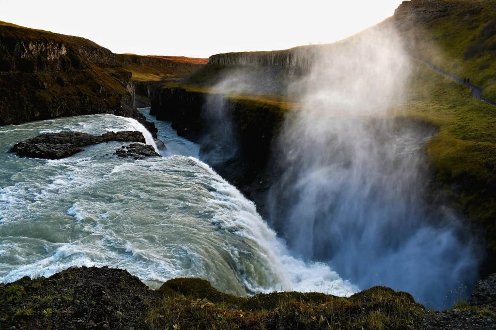 Breiter Wasserfall stürzt in tiefe Schlucht, erhebliche Gischt und grasbewachsene Klippen