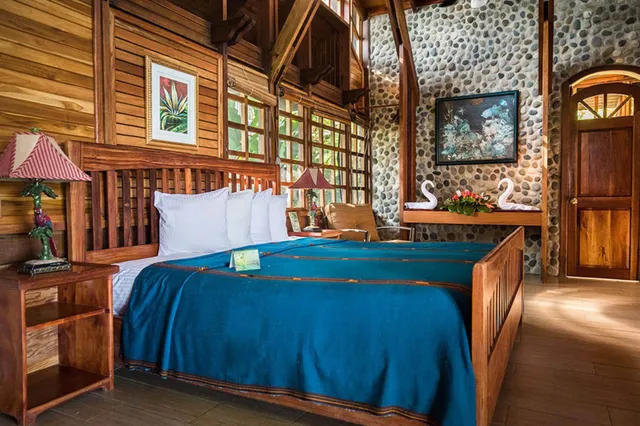 Gemütliches Holzschlafzimmer mit großem Bett, blauer Bettdecke, Steinwand und Handtuchschwänen