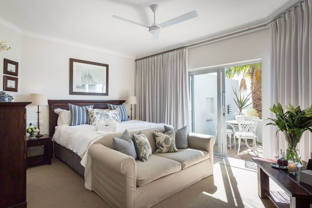 Helles Schlafzimmer mit Doppelbett, Sofa und sonniger Terrasse mit weißer Sitzgruppe