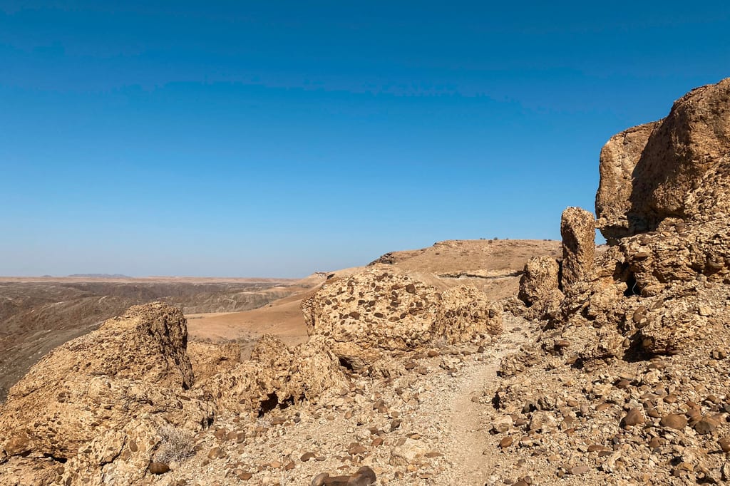 Felsige, trockene Wüstenlandschaft mit Pfad unter klarem blauem Himmel