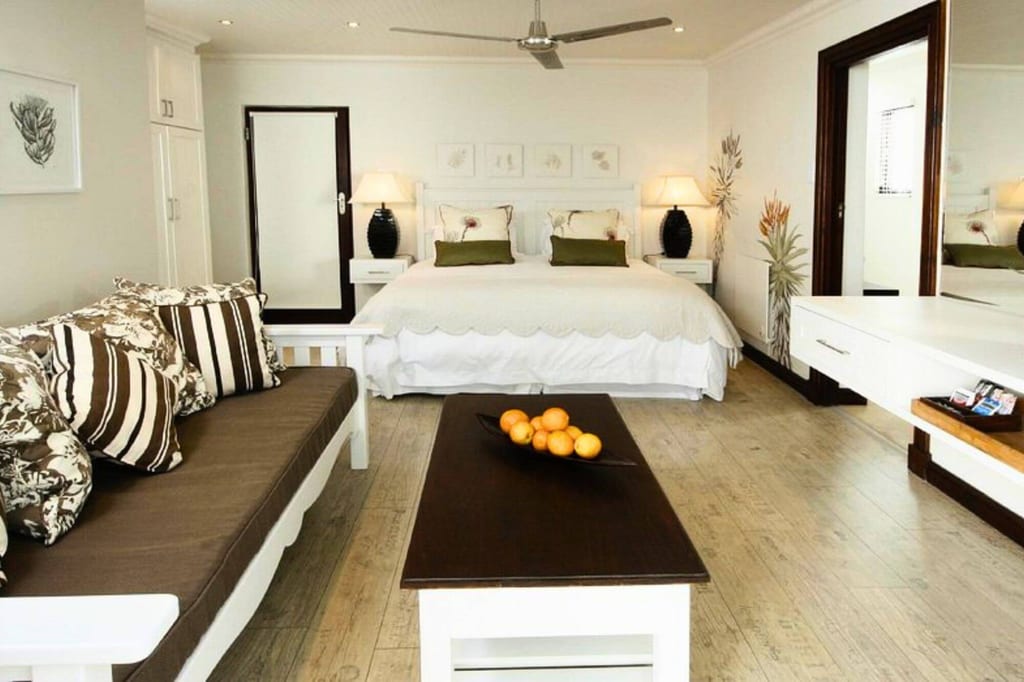 Helles Hotelzimmer mit Doppelbett, Sofa und Couchtisch mit Orangen, freundliche Tageslichtstimmung.