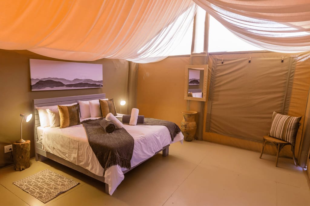 Innenansicht eines gemütlich eingerichteten Safari-Zeltes mit großem Bett und warmer Beleuchtung.