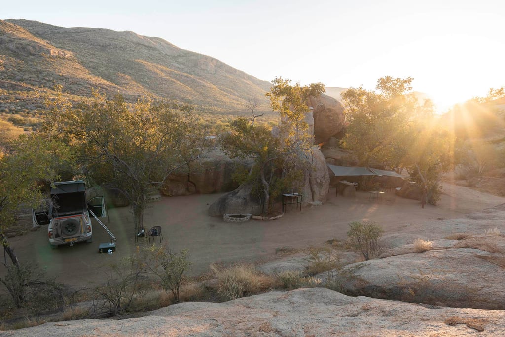 Camp mit Geländewagen und Felsformationen im warmen Licht der tief stehenden Sonne.