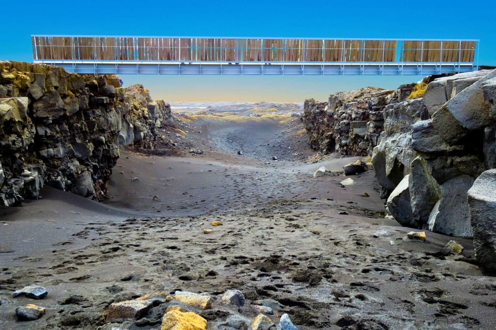Schmale Felsenschlucht mit schwarzem Sand und einer hölzernen Brücke darüber, Blick in die Tiefe.