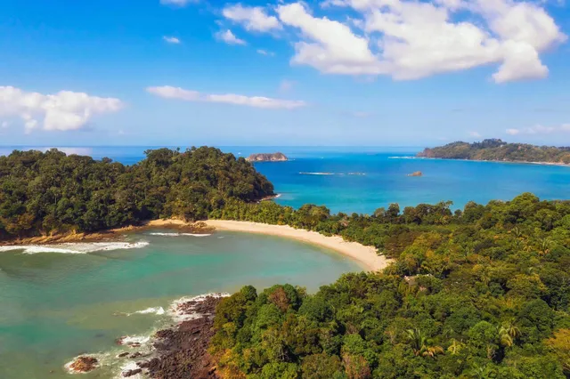 Luftbild einer Sandbucht mit türkisfarbenem Meer und dichtem Regenwald an der Küste Costa Ricas.