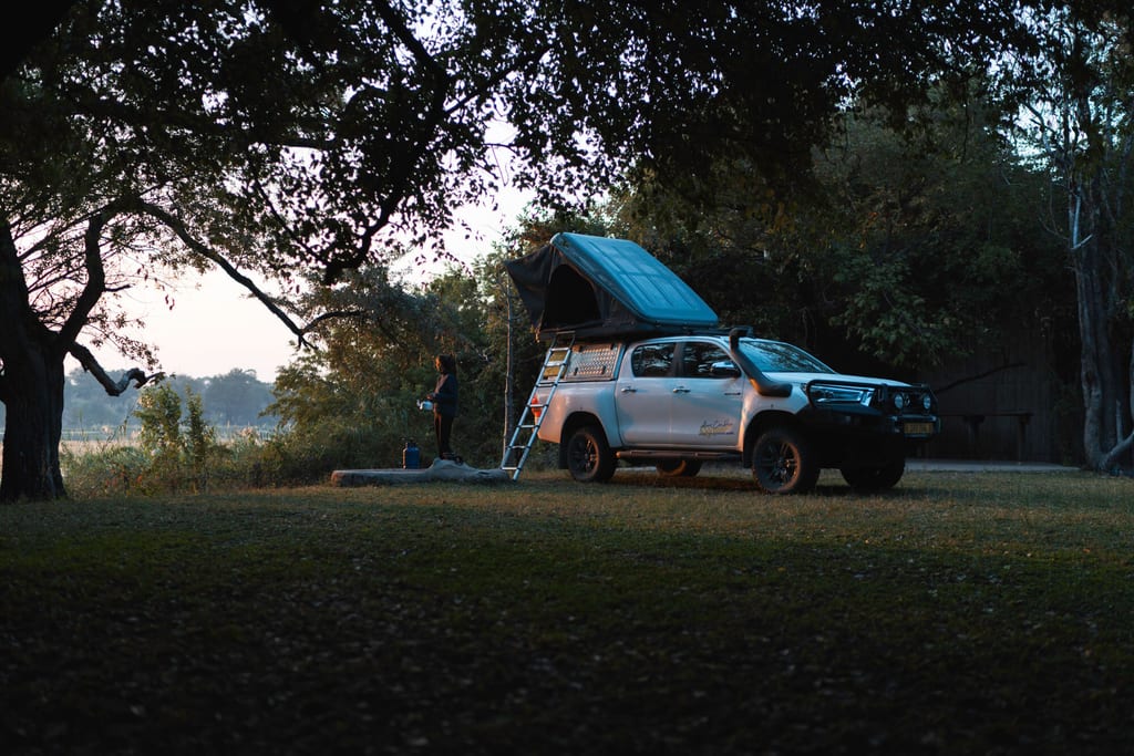 Geländewagen mit aufklappbarem Dachzelt auf Wiese bei Abendlicht, Person steht daneben.