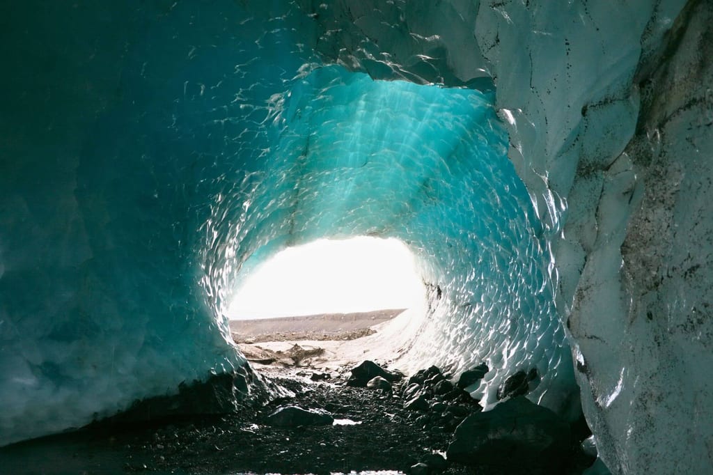 Blick aus einem blauen Eistunnel auf helle Außenfläche mit kiesigem Boden