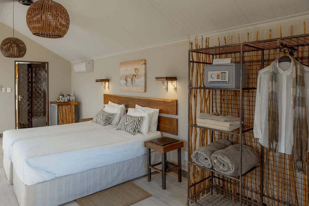 Hell eingerichtetes Doppelzimmer mit zwei Betten, offenem Regal und warmem Tageslicht.