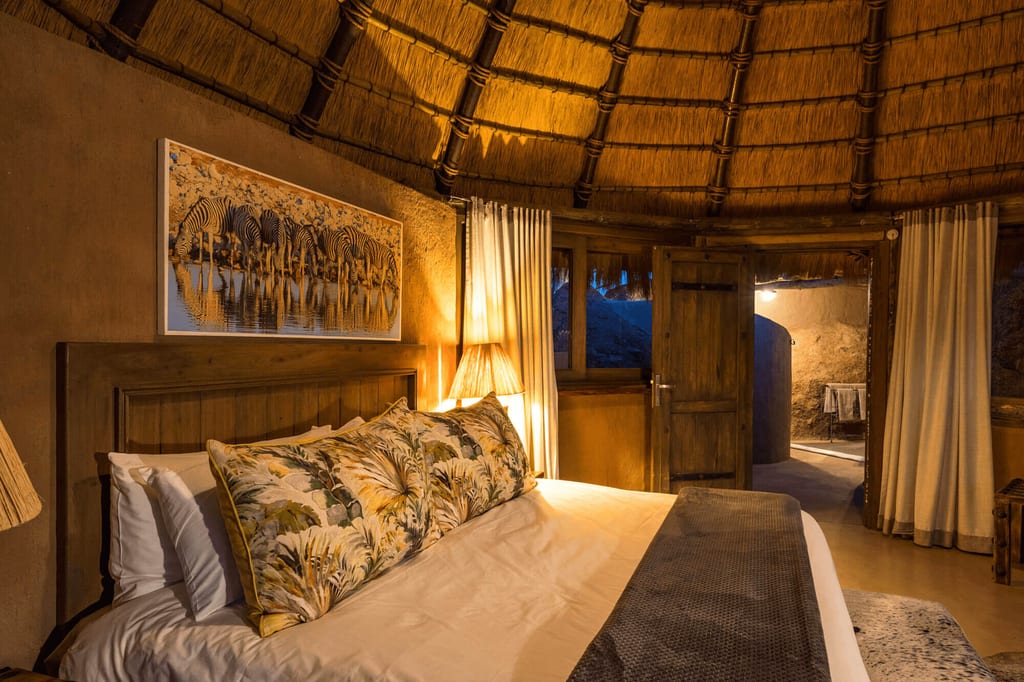 Gemütliches Schlafzimmer in Rundhütte mit Strohdach, warmem Abendlicht und geöffneter Holztür.