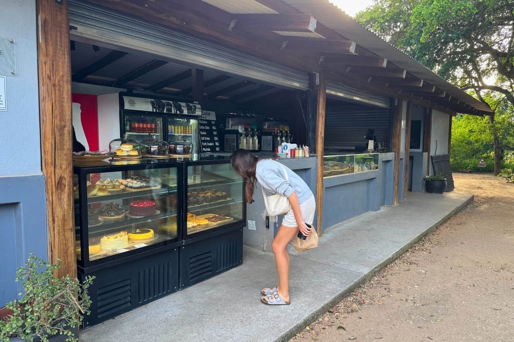 Person beugt sich an einem Kiosk vor einer Vitrine mit Kuchen in entspannter Spätnachmittagsstimmung.