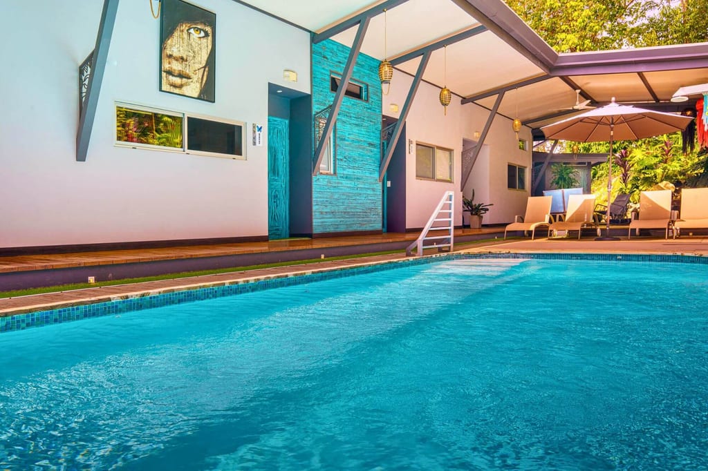 Niedrige Perspektive auf klares Schwimmbad mit Terrasse, Liegestühlen und Sonnenschirm am Nachmittag.