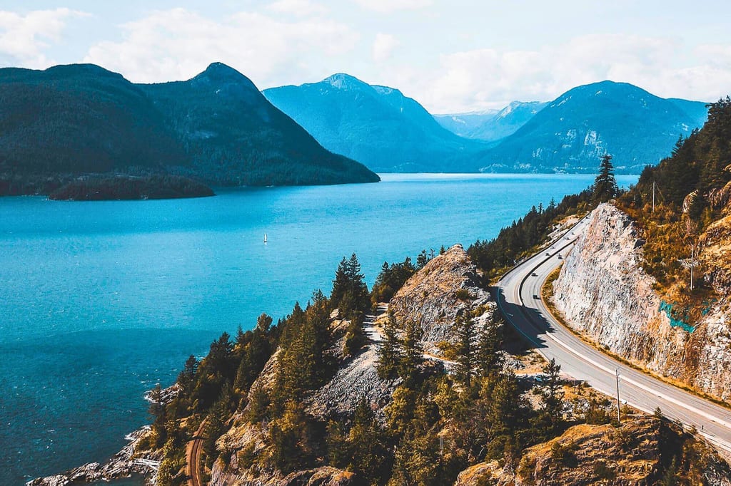 Aussicht auf Sea to Sky Highway an der kanadischen Küste mit Bergen, Straße und blauem Meer.