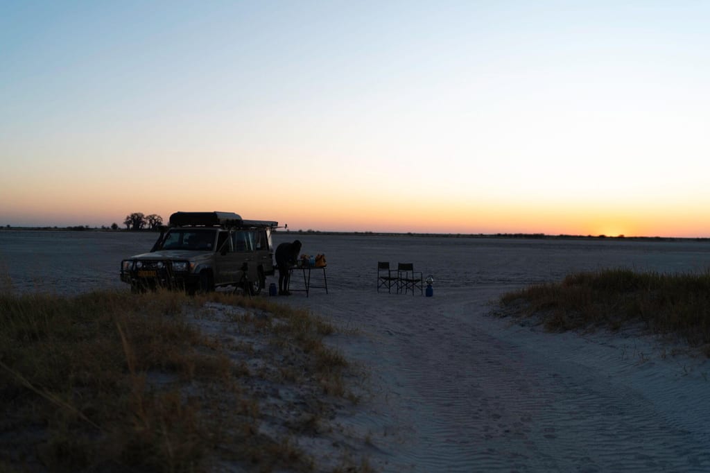Geländewagen und Campingausrüstung bei Dämmerung auf weiter Sandfläche mit ruhigem Abendhimmel