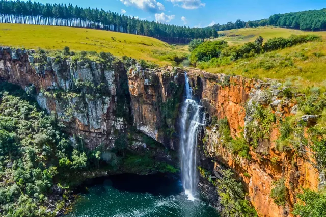 Luftaufnahme eines Wasserfalls, der von einer roten Felsklippe in ein dunkles Becken stürzt.