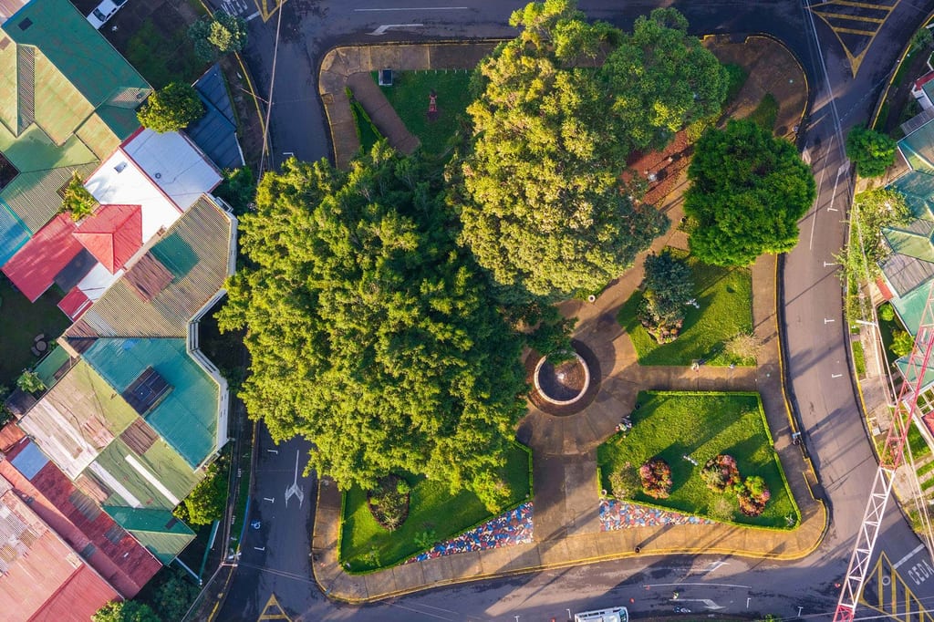 Luftaufnahme eines baumbestandenen Stadtparks mit Rundbrunnen, umgeben von bunten Dächern in San José, Costa Rica.