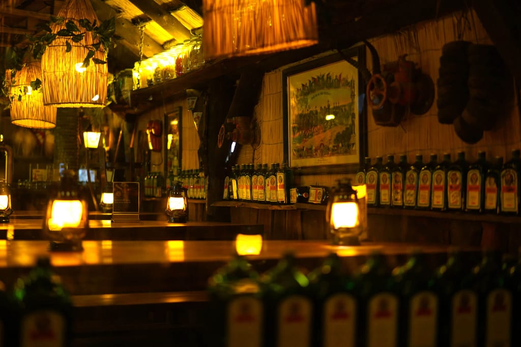 Rustikale Bar bei Laternenlicht mit Holztheke und Reihen von Flaschen, warme Abendstimmung.