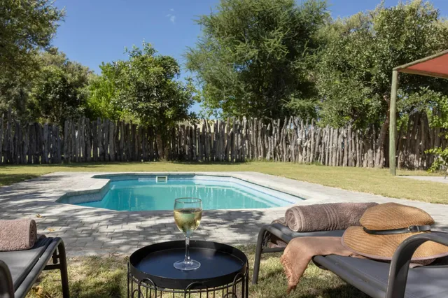 Pool im Garten mit zwei Liegen, Strohhut und Glas Weißwein bei sonnigem, blauem Himmel