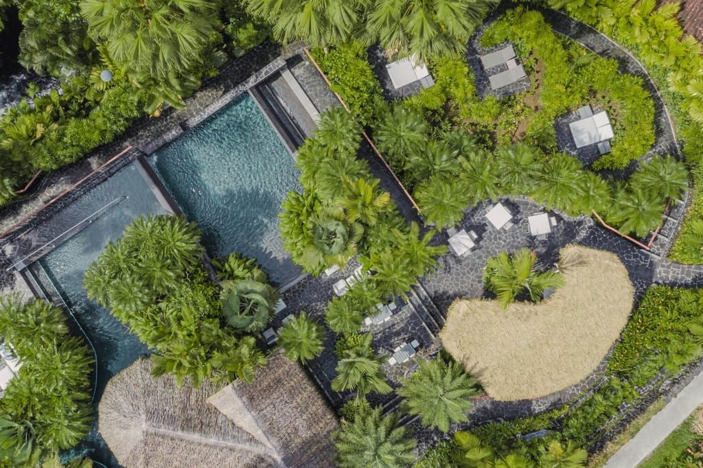 Vogelperspektive auf tropisches Resort mit Pools, Palmen, Wegen und Strohdächern